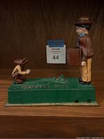 Side view showing man and monkey figures on green base with 'MONKEY BANK' embossed. Shows detailed hand-painted features and overall condition.