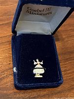 Front view of the Dresden dancer miniature inside the blue velvet box showing the figure's skirt and outstretched arms.