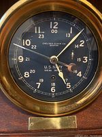 Front view of clock face showing black dial with 24-hour markings and brass bezel