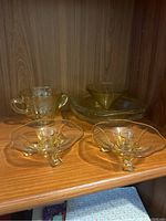 Full set of yellow Depression era glassware items displayed on a wooden shelf including teacups, candle holders, pitcher, and bowl.