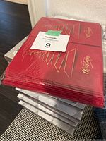 Stack of red Christmas card packs with gold embossed Christmas tree design and text, sealed in plastic.