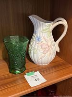 Photo showing both the Fitz & Floyd vintage ceramic floral pitcher and the green Anchor Hocking textured glass vase side by side on a wooden shelf.