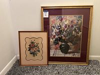Two framed floral prints leaning against a wall on carpeted floor, showing both large and small prints