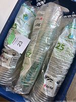 Eight sealed packs of Fabri-Kal Green Ware disposable cups in a bin, each pack labeled with 25 count and 24 oz capacity