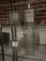 Stacked assorted size clear plastic food storage pans including True brand and generic, some with visible brand markings, stored on metal shelving.