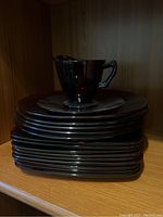 Stack of ruby red plates with one cup on top shown in shelf.