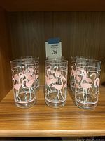 Six vintage Libbey glass tumblers on a wooden shelf, each decorated with pink flamingos around the sides.