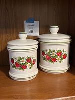 Two vintage Sears ceramic canisters decorated with strawberry, leaf, and blossom designs on a white base, with green trim accents and round knob lids.