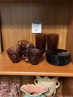 Six amethyst purple swirl glass teacups and six matching saucers, two additional saucers, and two tumblers on a wooden shelf.