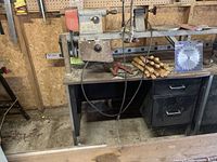 Full view of 10-inch metal lathe mounted on metal desk with drawers, showing lathe bed, headstock, and tailstock, also some wooden-handled turning tools on desk surface.