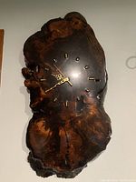 Photo of a wall clock made from a polished natural burl wood slab with gold decorative hands and hour markers.
