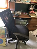 Black mesh office chair with armrests and wheels positioned next to the desk