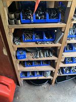 Photo showing wooden shelves with multiple blue bins filled with various metal nuts, bolts, washers, clamps, and fittings.