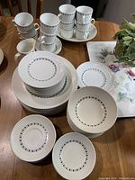 Photo of assembled white ceramic plates and cups with black rectangular pattern stacked on a wooden table.