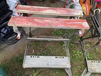 Saw horse with red wooden tops on metal frame, plastic footrest visible, dirty and used condition