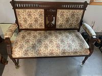 Front view of wood frame settee with floral upholstery and padded armrests.