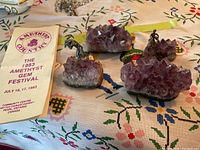 Four amethyst pieces with two metallic figures, set on embroidered cloth with informational pamphlet from 1983 Amethyst Gem Festival.