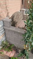 Side view showing resin bench backrest with decorative emblem and pillar-style armrest, placed against brick wall and stone tiled base.