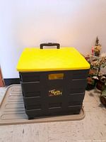Front view of large black plastic Quik Cart storage cage with yellow lid and handle