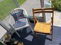 Photo shows white plastic garden chair with blue-red striped removable cushion next to light wood folding chair on porch.