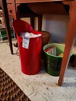 Photo of tall red metal coal bucket with handle, green glazed ceramic pot, and medium brown wicker basket under wooden table