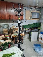 Front view of a black metal coat tree with multiple tiers of hooks, located in a basement with concrete block walls and other stored items.