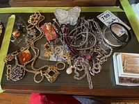 Display of assorted costume jewelry on dark surface, showing multiple necklaces, bangles, brooches, rings, and earrings in various styles and metal finishes.