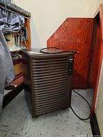 Kenmore dehumidifier shown in a corner on tiled floor, brown plastic exterior with vent grille and control panel visible.