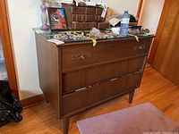 Front and side view of a vintage wooden dresser showing three drawers and a glass top, situated on a hardwood floor.