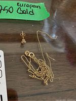 Chain and single stud earring on wooden surface with green “750 European Gold” label