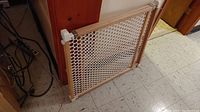 Photo showing the wood framed safety gate with plastic mesh, positioned on floor leaned against a cabinet.