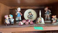 Shelf view showing Goebels figurines including boy with rifle, girl with basket, pairs of children, decorative roses, and bell.