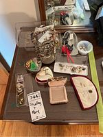Overall lot with earrings on stand, small trinket boxes, pins, and other jewelry pieces displayed on a dark wood table surface