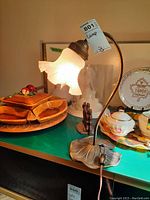 Full view of the table lamp showing the frosted glass ruffled lampshade and curved stem on a detailed leaf base.