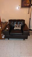 Front view of dark brown tufted armchair with decorative pillow on seat.