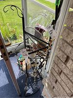 Iron black plant stand with three triangular shelves, rust and weathering visible, displayed in a glass porch area with no contents included.