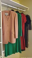 Five garments on hangers: pink jacket, green dress, red dress, dark multicolored dress