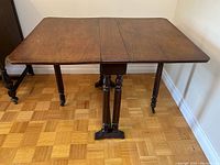 Full view of the drop leaf table with both leaves extended showing wooden surface and turned legs with casters.