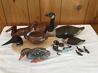 Overview of the duck lot including multiple wooden and pottery duck figurines arranged on a white cloth with wood backdrop.