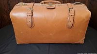 Full front view of the light brown leather bag showing two buckle straps and scuff marks.