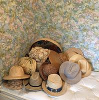 Photo showing 13 hats arranged on a bed, variety of straw hats with different styles and weaves