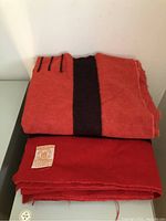 Two folded red Hudson's Bay wool point blankets stacked, one showing central dark stripe