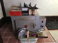Front view of gray electric kiln with control box on right side, handle on door and tools resting on top and in front