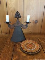 Photo of the bronzed metal candle holder shaped like a woman in folk costume holding two candles alongside the decorative round wooden folk art plate.