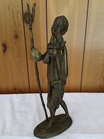 Full view of bronze sculpture showing standing figure with staff and curved container