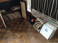 Photo showing vinyl records stored in wooden shelves and boxes by a window with metal railings