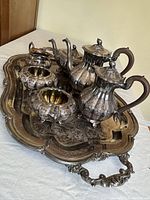 Side angled view of the entire silver plated tea and coffee service set on the ornate tray showing the teapots, creamer, sugar bowls.