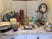 Overview of all vintage vanity items on marble countertop including perfume bottles, razors, toiletry bags, decorative items, and grooming accessories.
