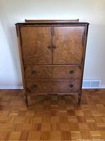 Front view of vintage walnut high boy dresser showing two cabinet doors above two drawers with metal handles and decorative details on legs and edges.