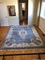 Full view of the 8x10 wool area rug laid out on floor under natural light, showing blue background with floral pattern and fringe ends.